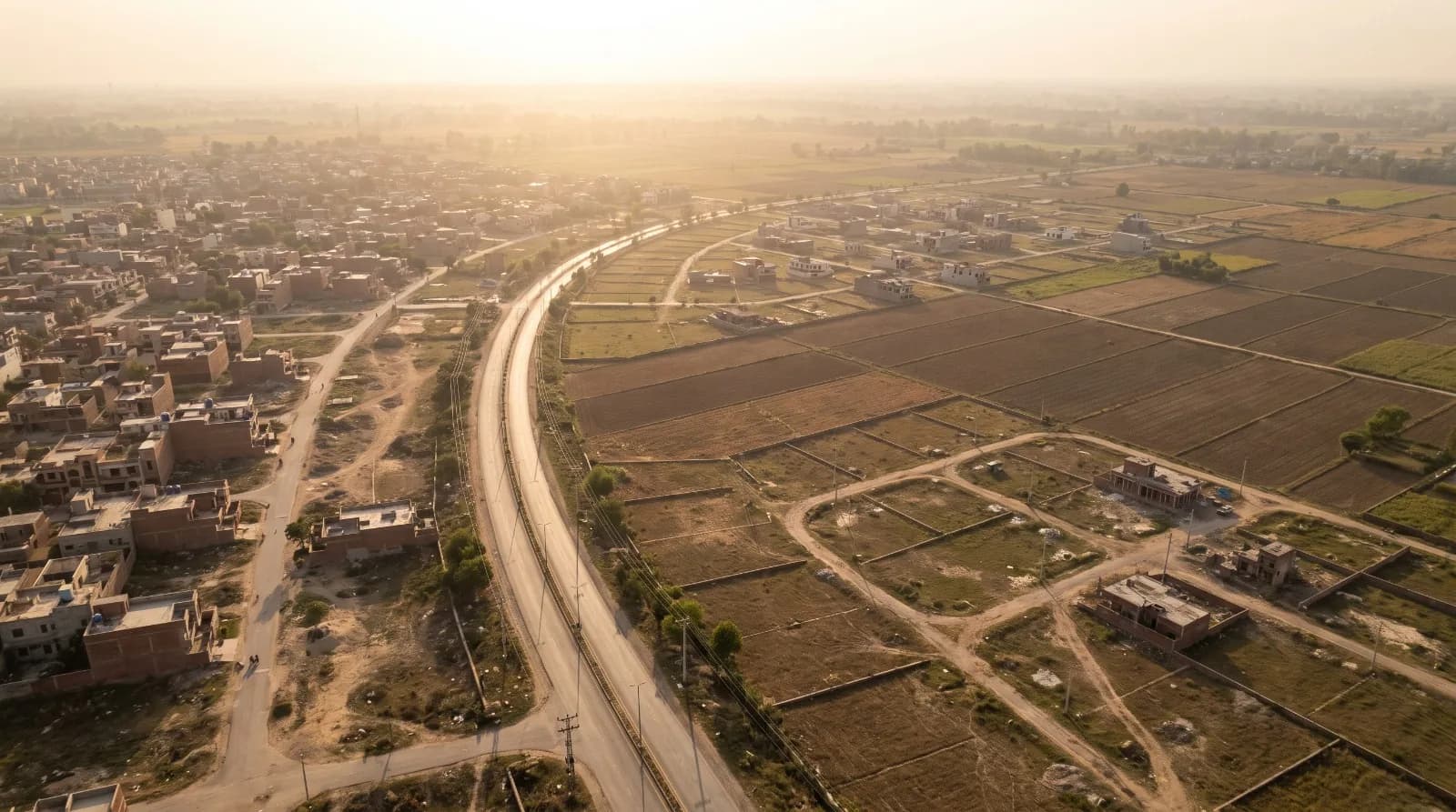 Aerial view showing the transition between a low-rise neighbourhood, roads and agricultural land around Lahore.